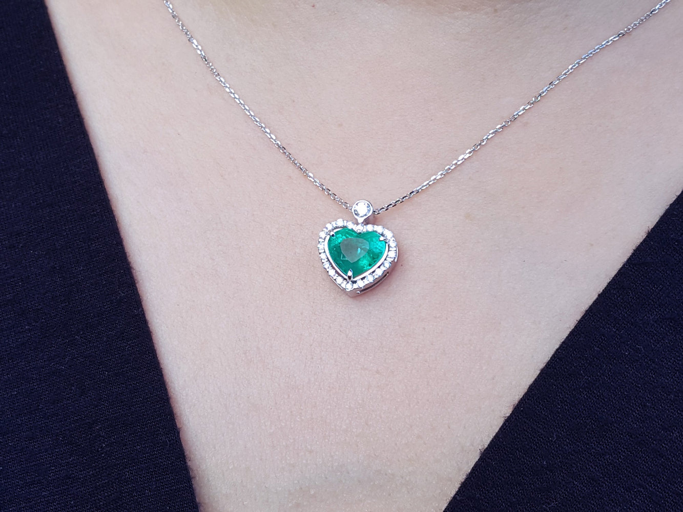 Heart-shaped emerald pendant on a white gold chain on a person&#39;s neck