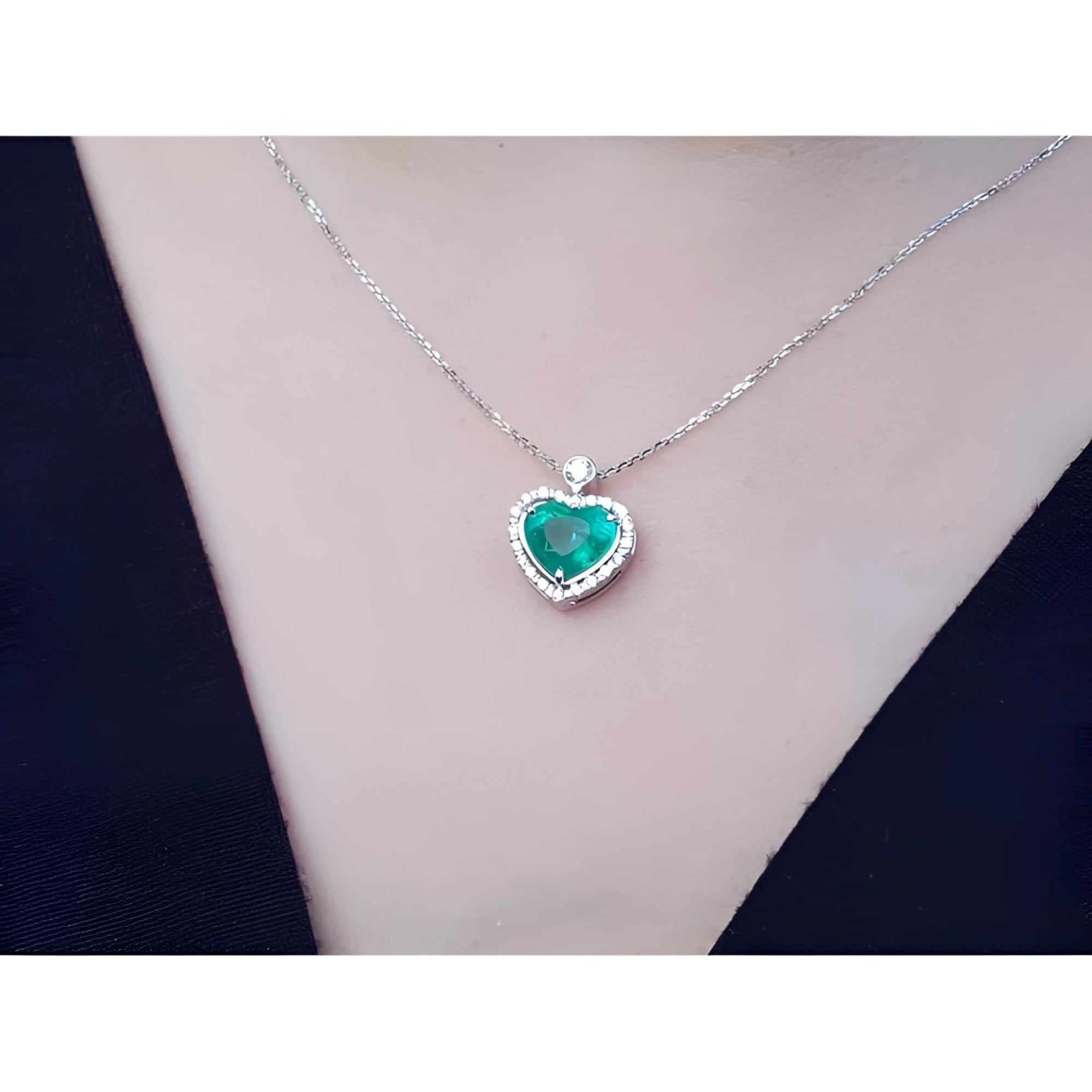 Natural emerald heart pendant in 14K white gold with diamond halo on a delicate chain, worn on a person.