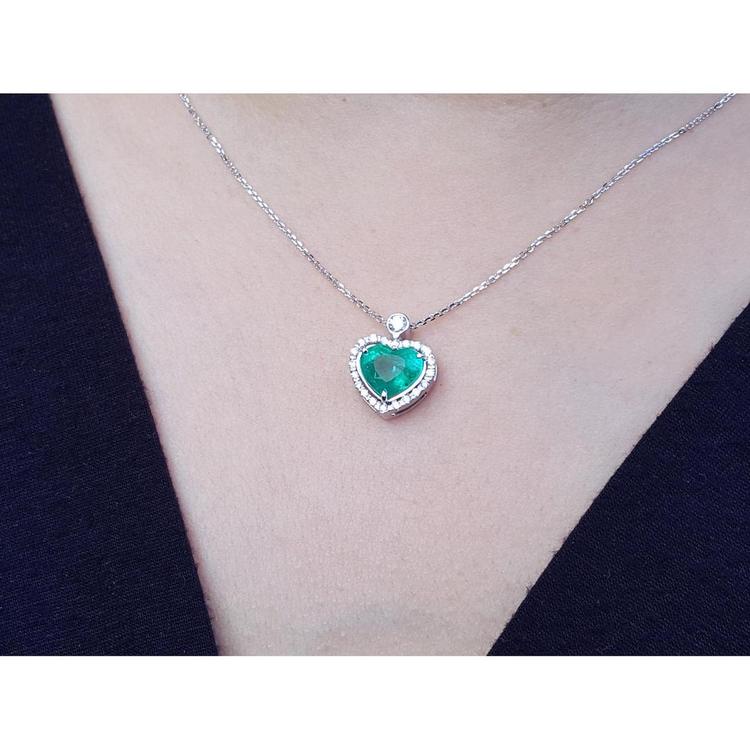 Heart-shaped emerald pendant on a white gold chain on a person's neck