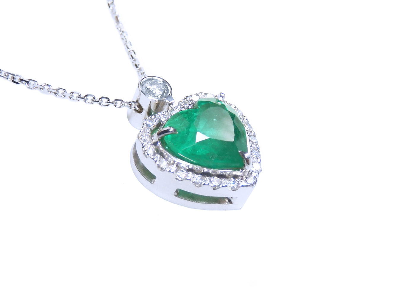 Heart-shaped emerald pendant with diamond accents on a toside anda gallery profile view.