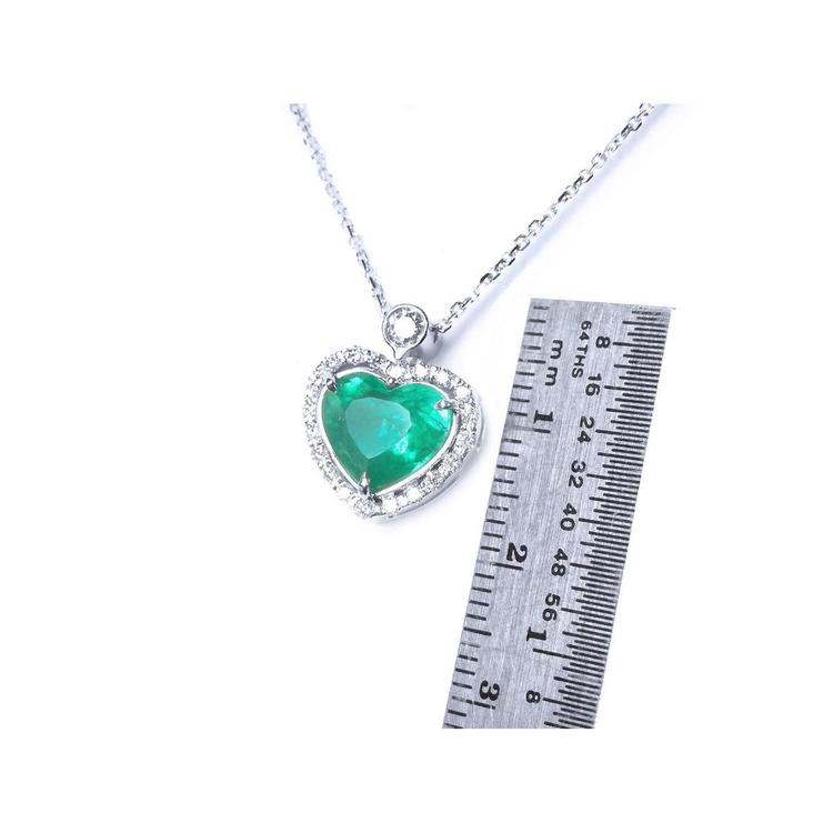 Heart-shaped emerald pendant on a chain with a ruler for scale on a white background.