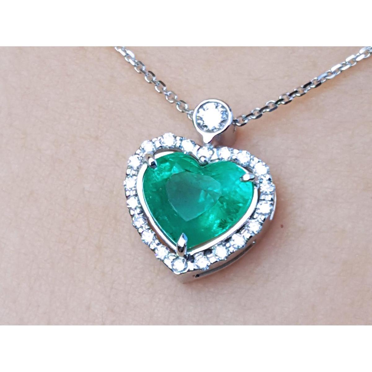 Heart-shaped emerald pendant with diamond accents on a silver chain topside view.