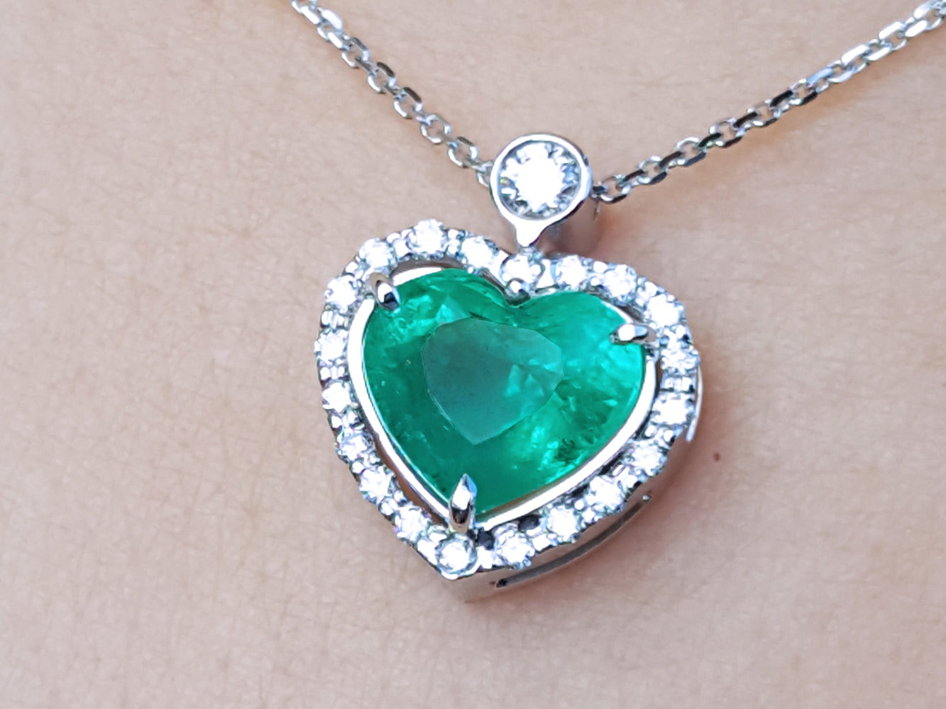 Heart-shaped emerald pendant with diamond accents on a silver chain topside view.