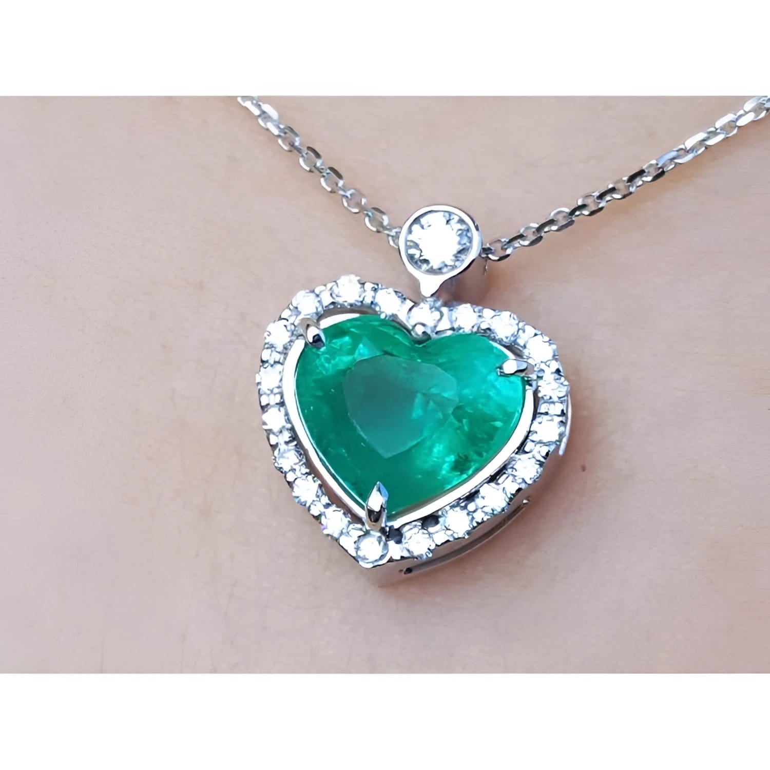 Heart-shaped emerald pendant with diamond accents on a silver chain topside view.