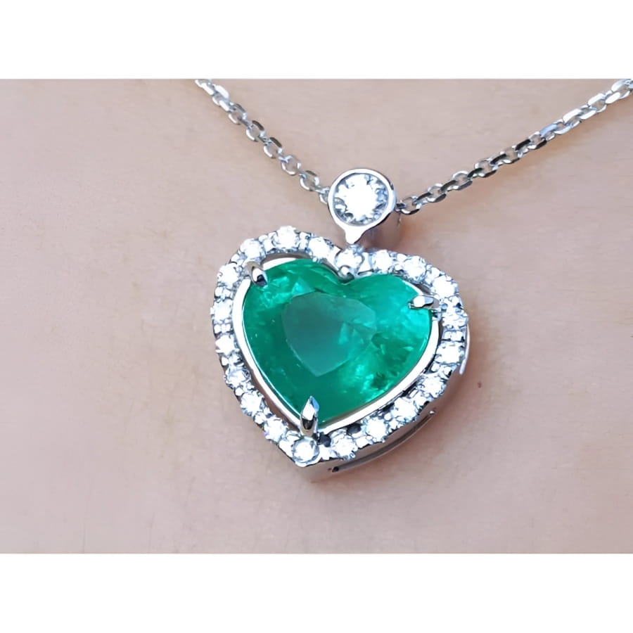 Heart-shaped emerald pendant with diamond accents on a silver chain topside view.