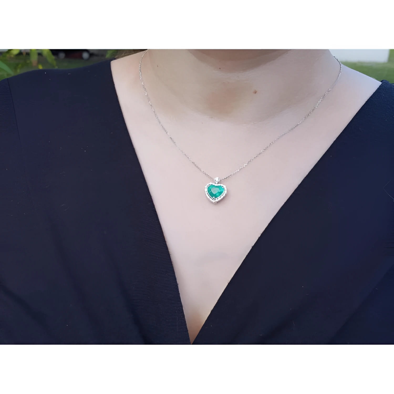 Emerald heart pendant in 14K white gold with diamonds, worn on a woman's neck.
