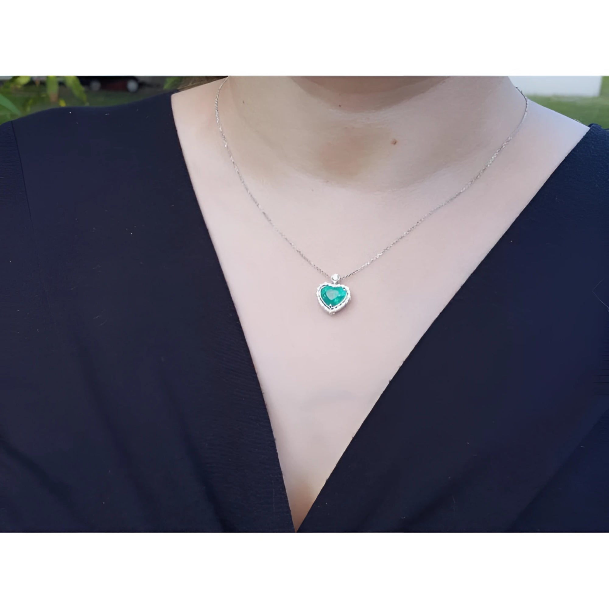 Emerald heart pendant in 14K white gold with diamonds, worn on a woman's neck.