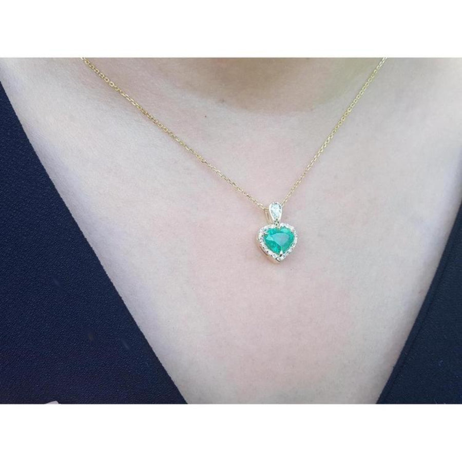 Heart-shaped emerald and diamond halo pendant in 14K yellow gold on a woman's neck.