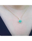 Heart-shaped emerald and diamond halo pendant in 14K yellow gold on a woman's neck.
