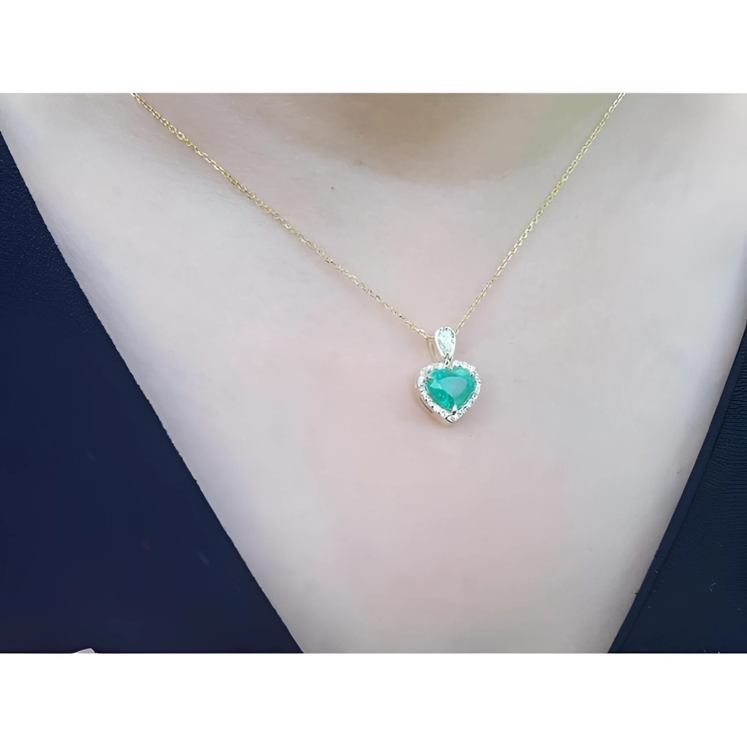 Heart-shaped emerald and diamond halo pendant in 14K yellow gold on a woman's neck.
