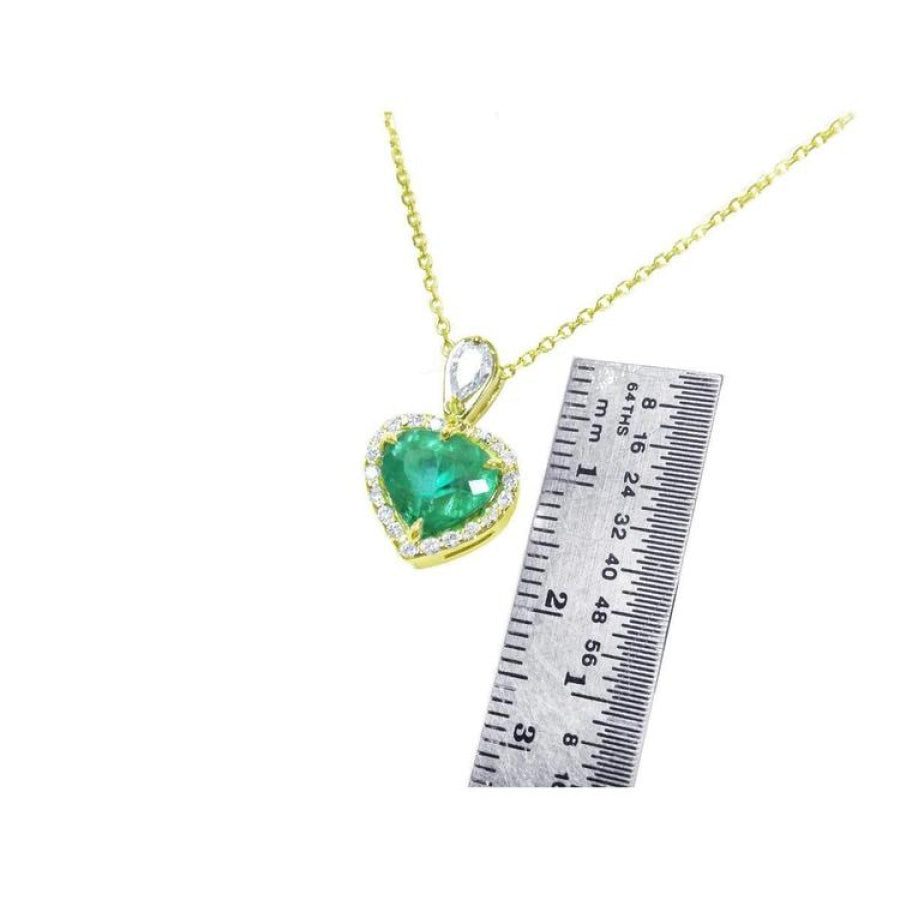 14K yellow gold heart pendant with a deep green emerald and diamond halo, next to a ruler.