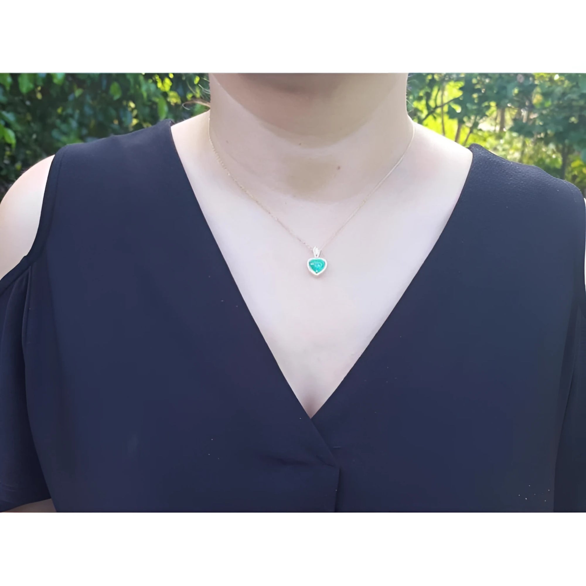 Heart-shaped emerald and diamond pendant in 14K yellow gold, worn on a woman's neck.