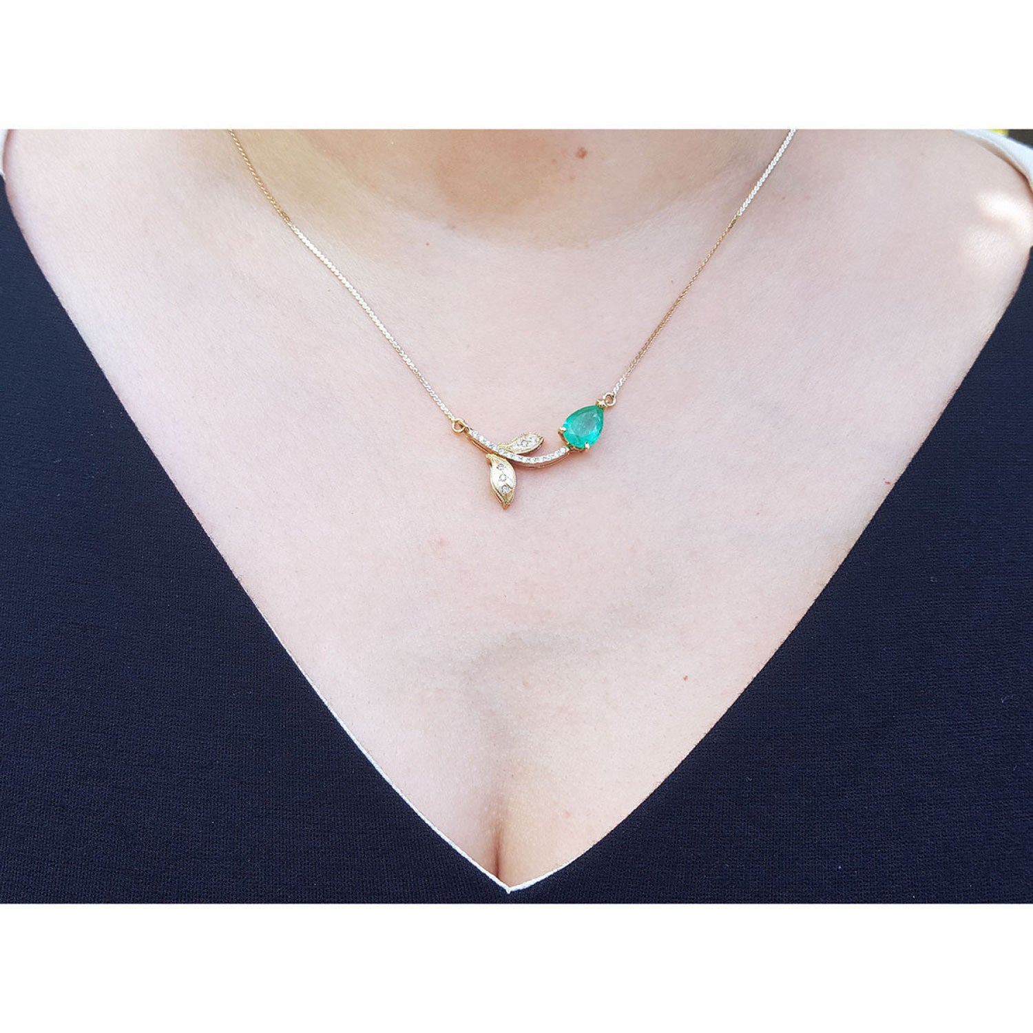 14K yellow gold twig necklace with a pear-cut natural emerald and diamond leaves on a woman's neck.