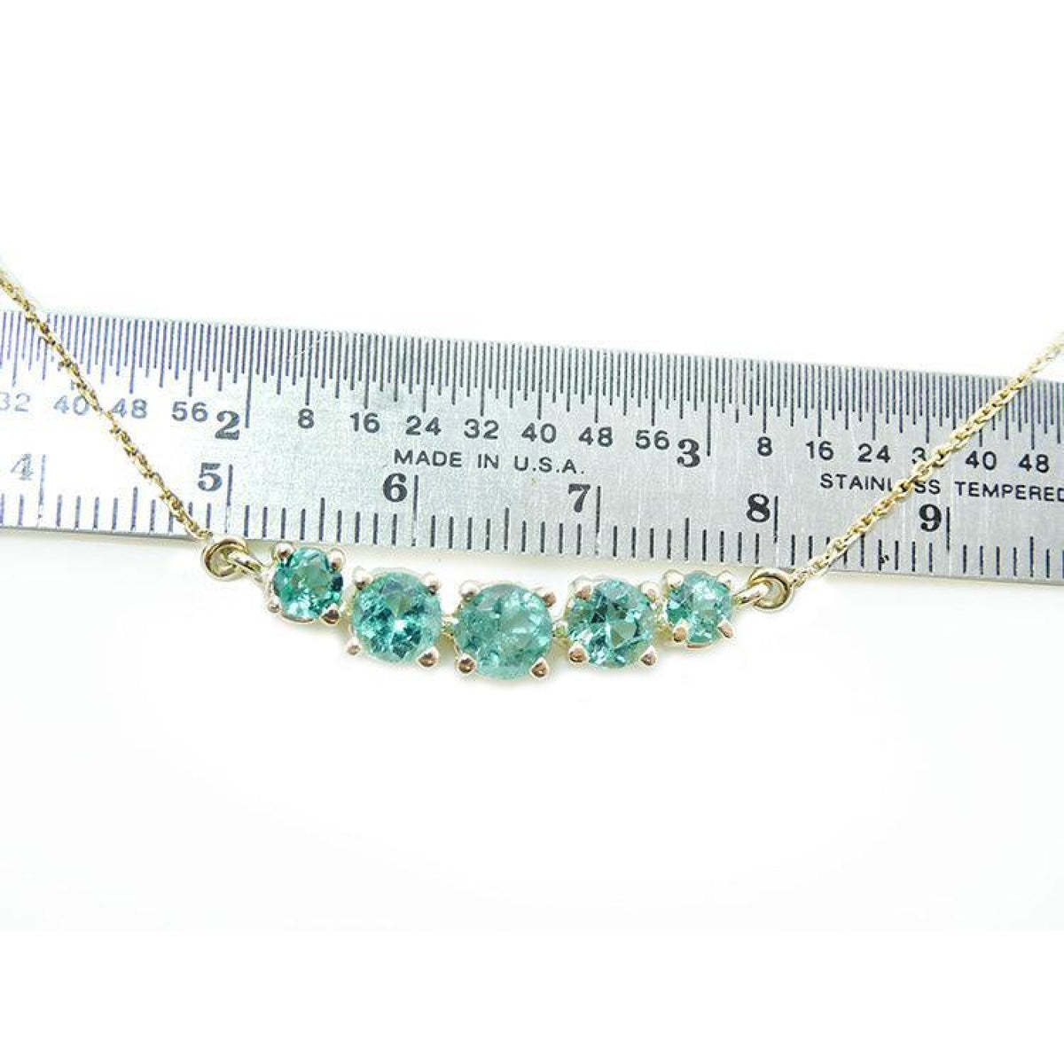 14K gold necklace with five round, medium light green Colombian emeralds, varying in size, displayed against a ruler.