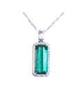Elongated natural emerald pendant with halo diamonds on an 18K white gold chain.