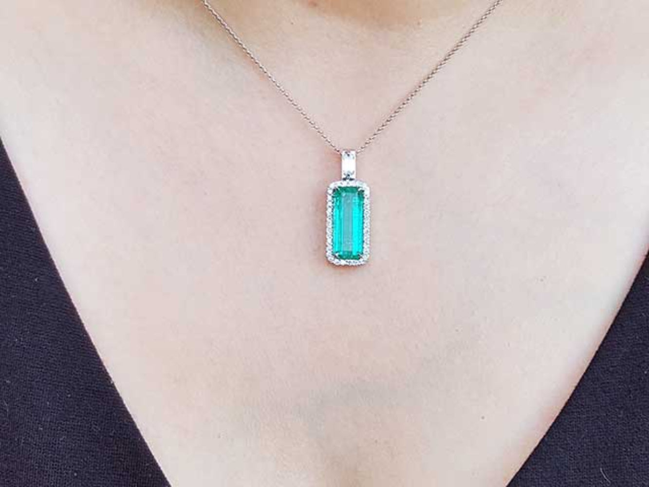 Green emerald pendant on a necklace against a black background
