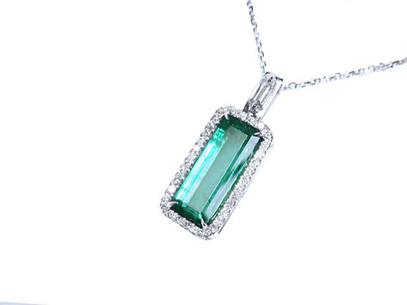 The topside view of a natural emerald pendant with halo diamond on a white background