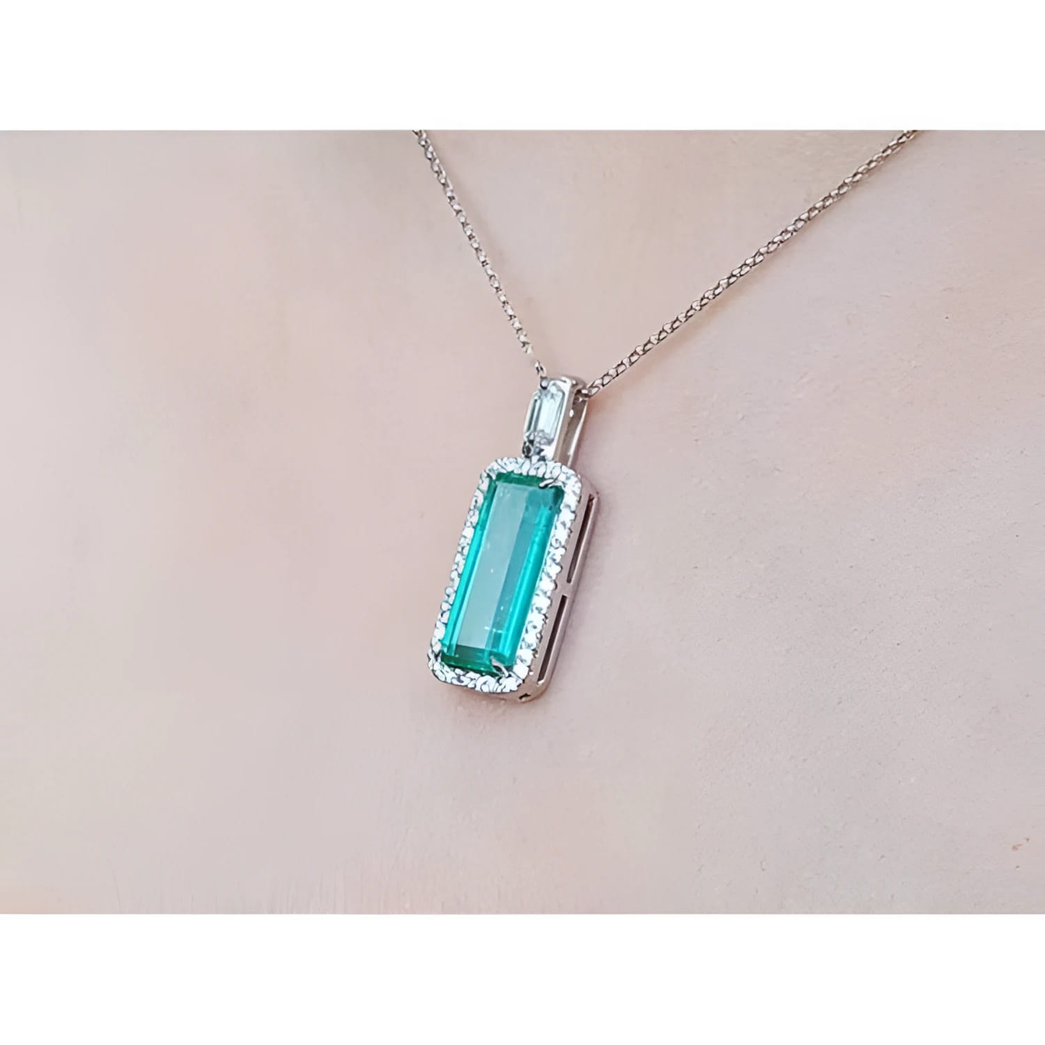 Elongated natural emerald pendant with halo diamonds in 18K white gold on a chain.