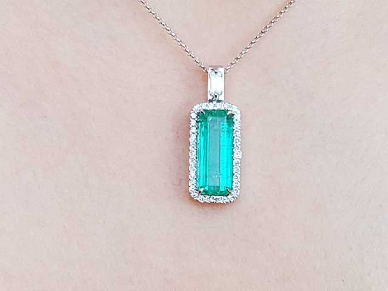 Green emerald pendant necklace on a light pink background