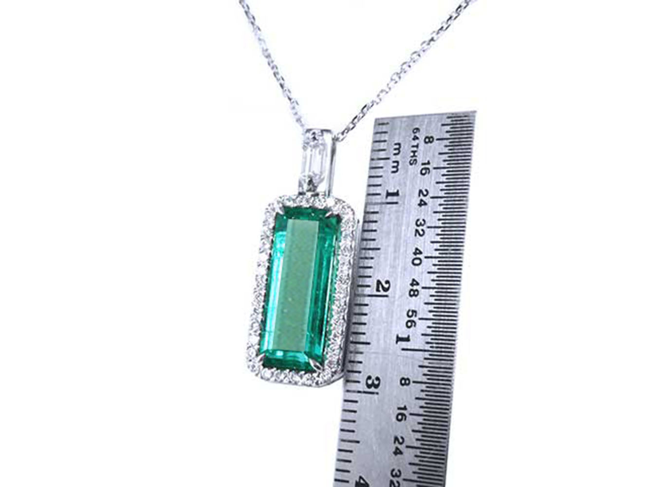 Genuine Colombian emerald pendant with white gold chain with a ruler for scale on a white background