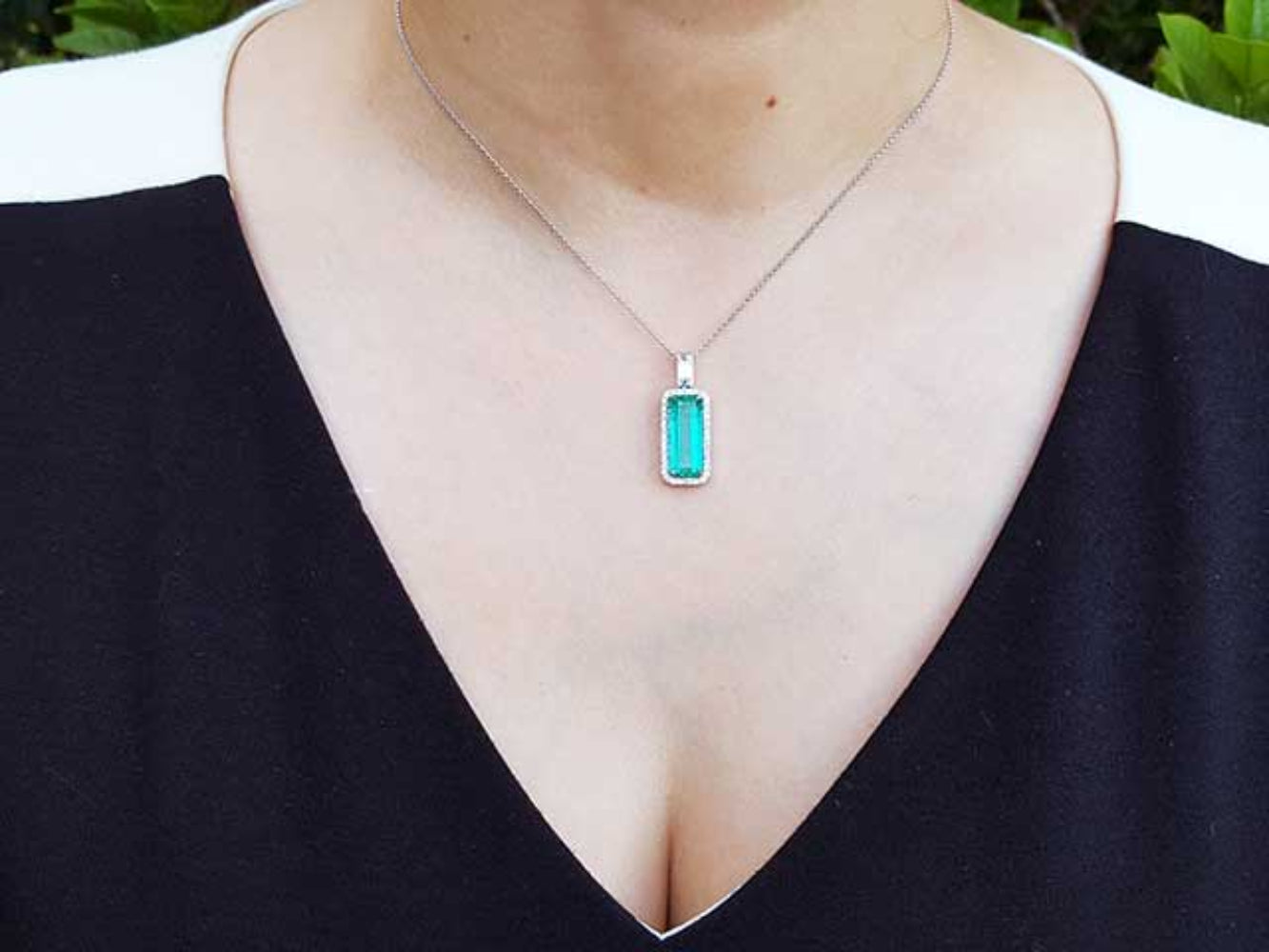 Necklace with a colombian emerald pendant worn by a person in a black top.