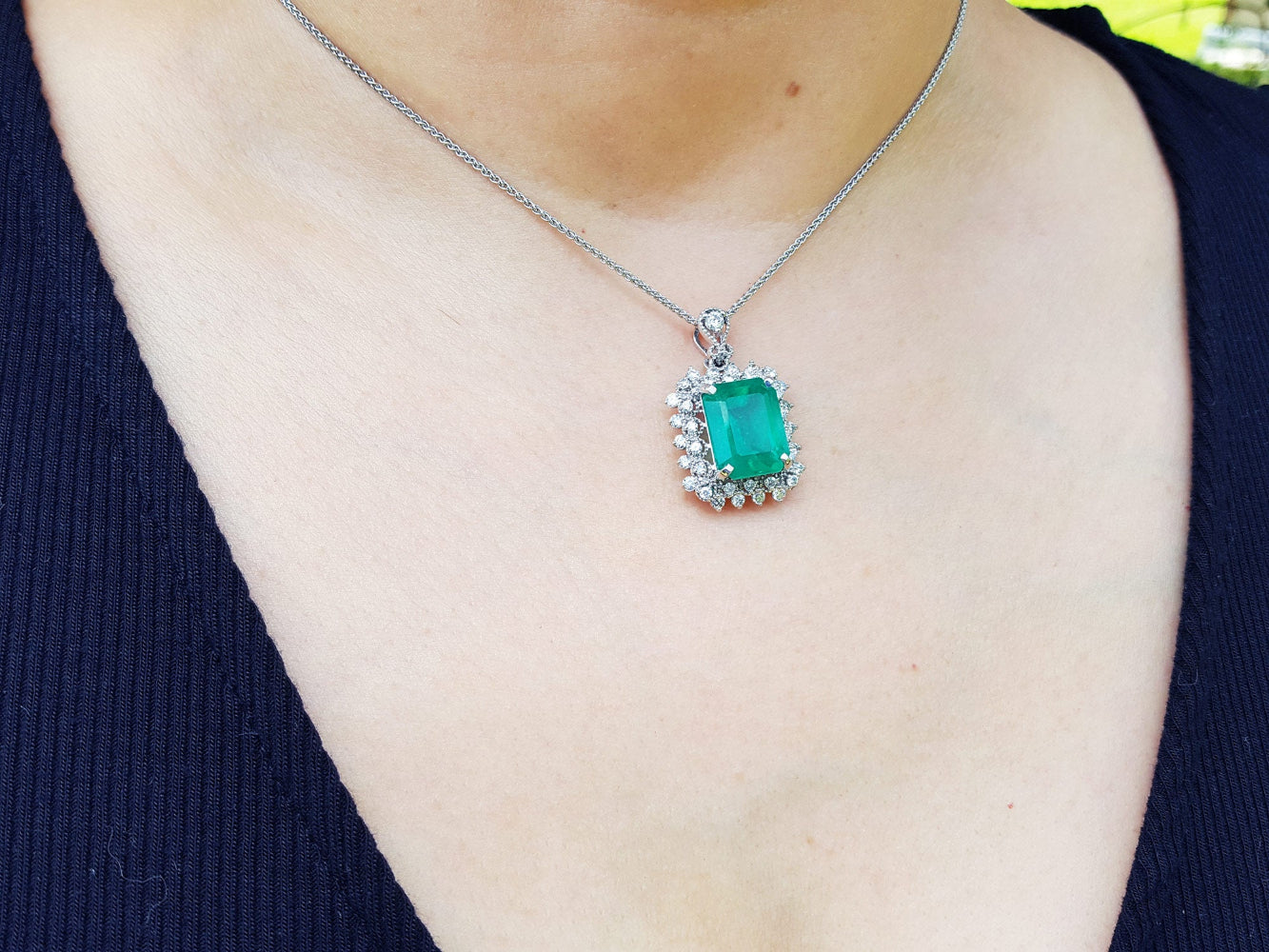 A person wearing a natural emerald pendant on a white gold chain 