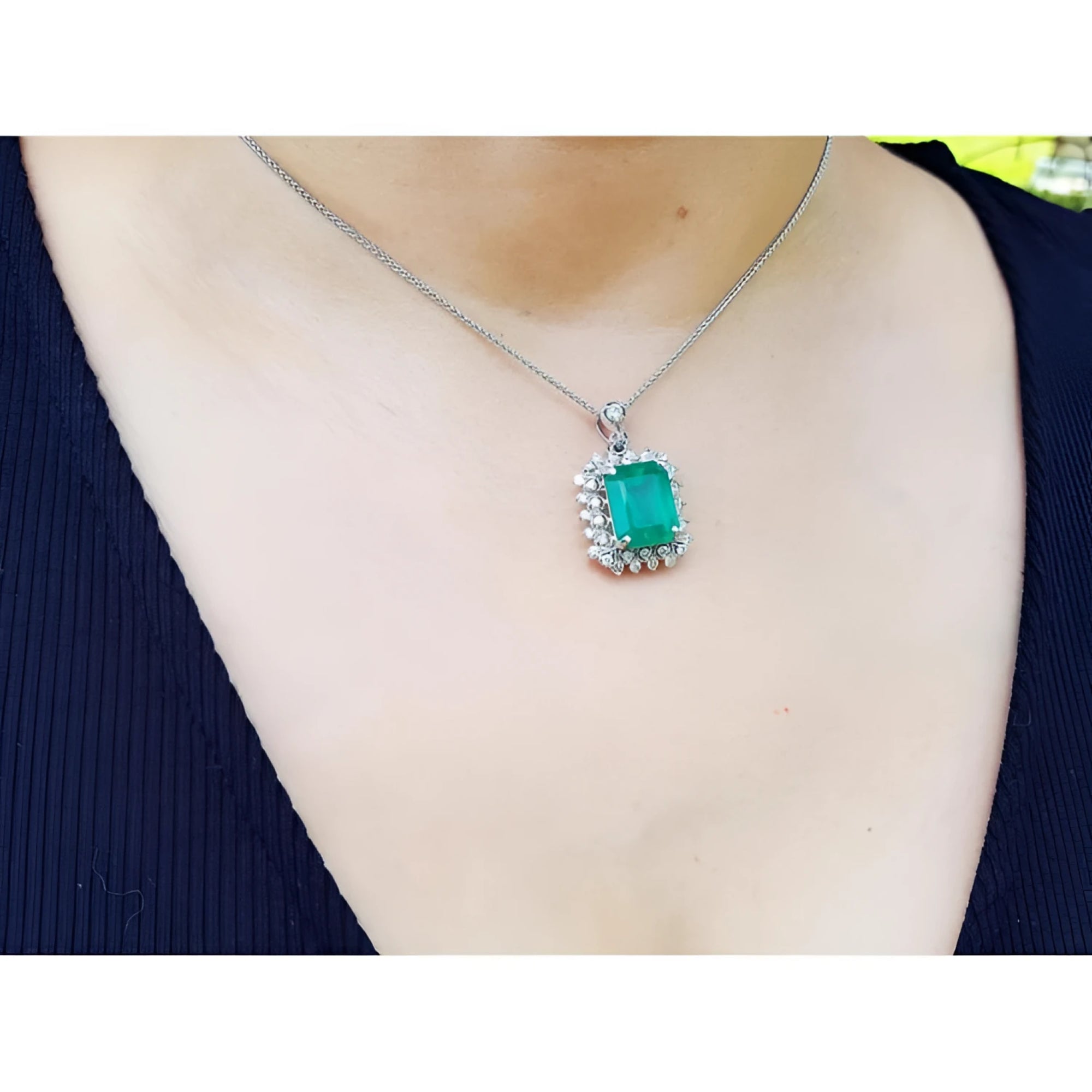 7.78 ct. natural emerald pendant with halo diamonds in 14K white gold, worn on a necklace.
