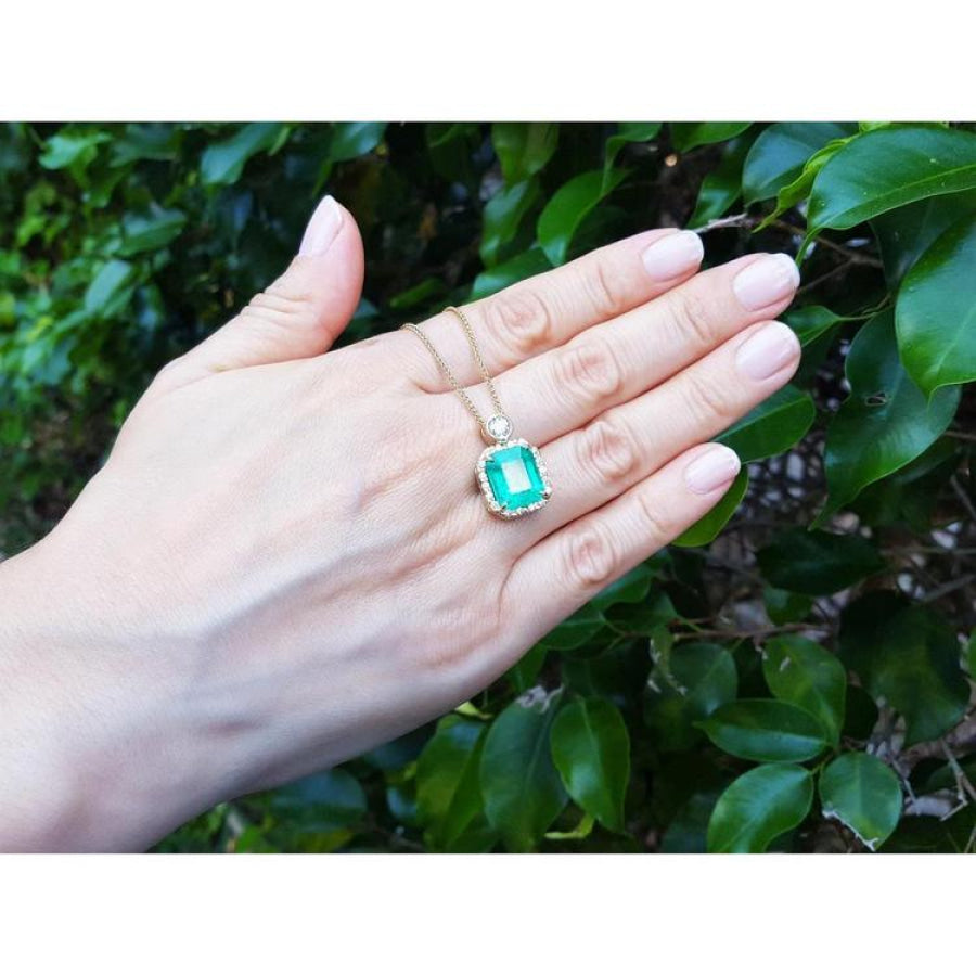 18K yellow gold pendant necklace with a rectangular emerald and diamond halo, held by a hand.
