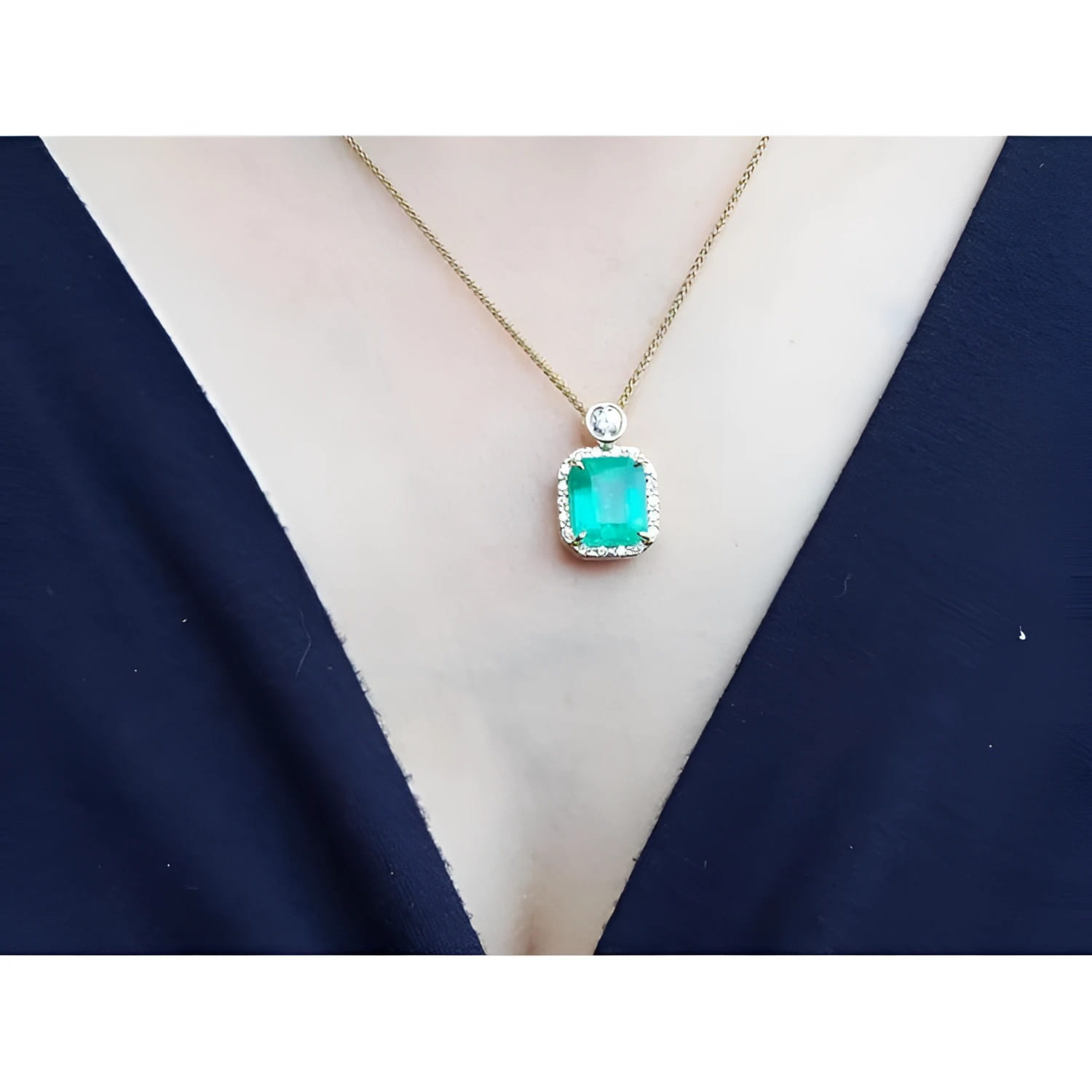7.09 ct. natural emerald pendant necklace with halo diamonds on an 18K yellow gold chain.