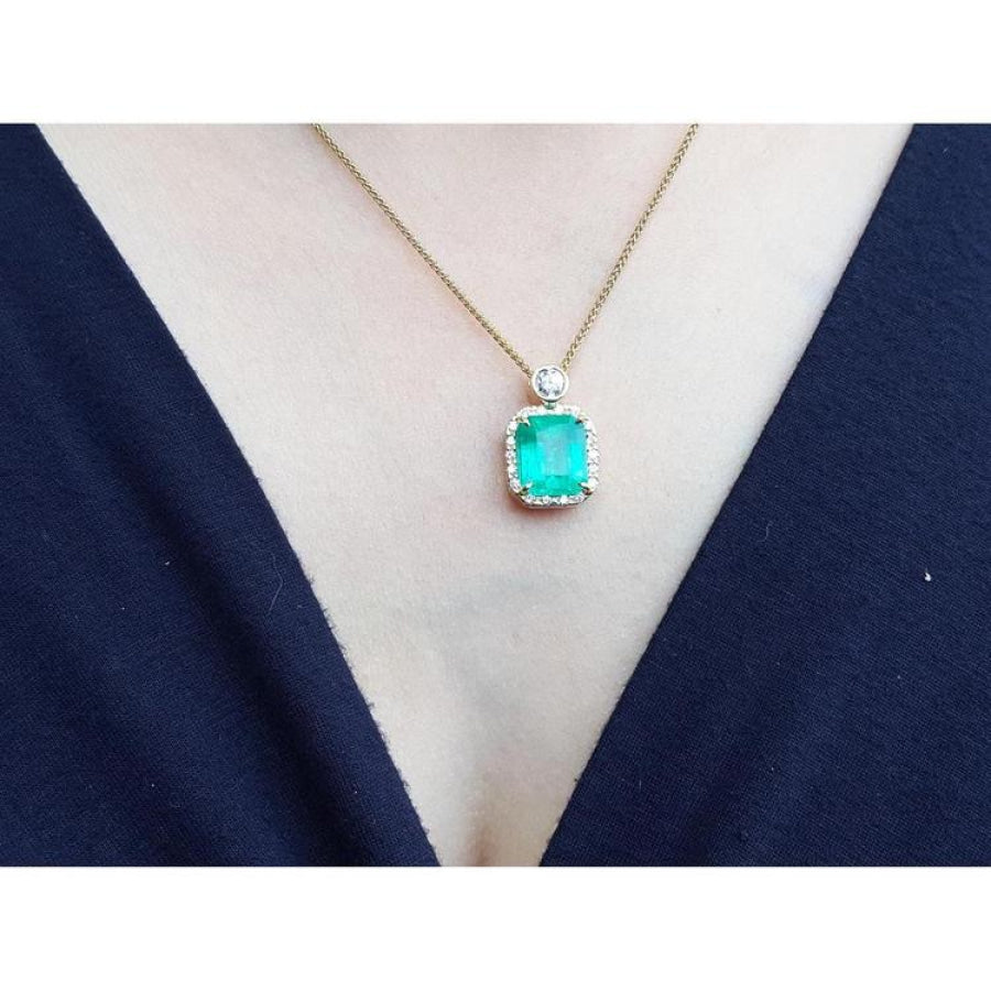 7.09 ct. natural emerald pendant necklace with halo diamonds on an 18K yellow gold chain.