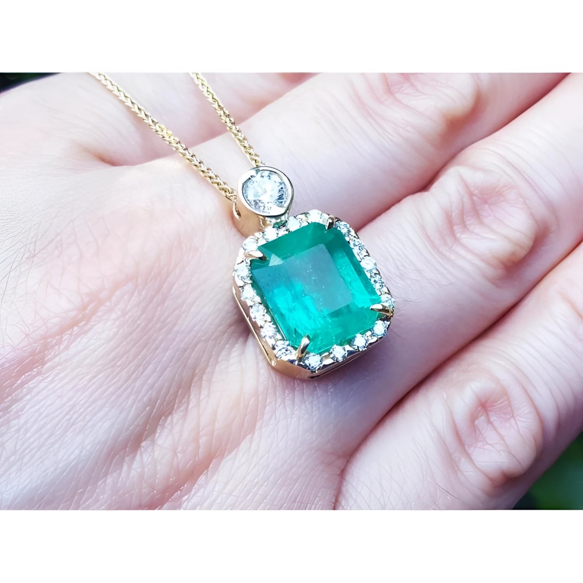 7.09 ct. natural emerald pendant necklace with halo diamonds on an 18K yellow gold chain.