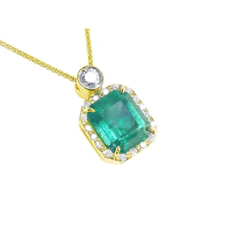 A 18k yellow gold pendant with a natural emerald and diamond accents on a topside view.