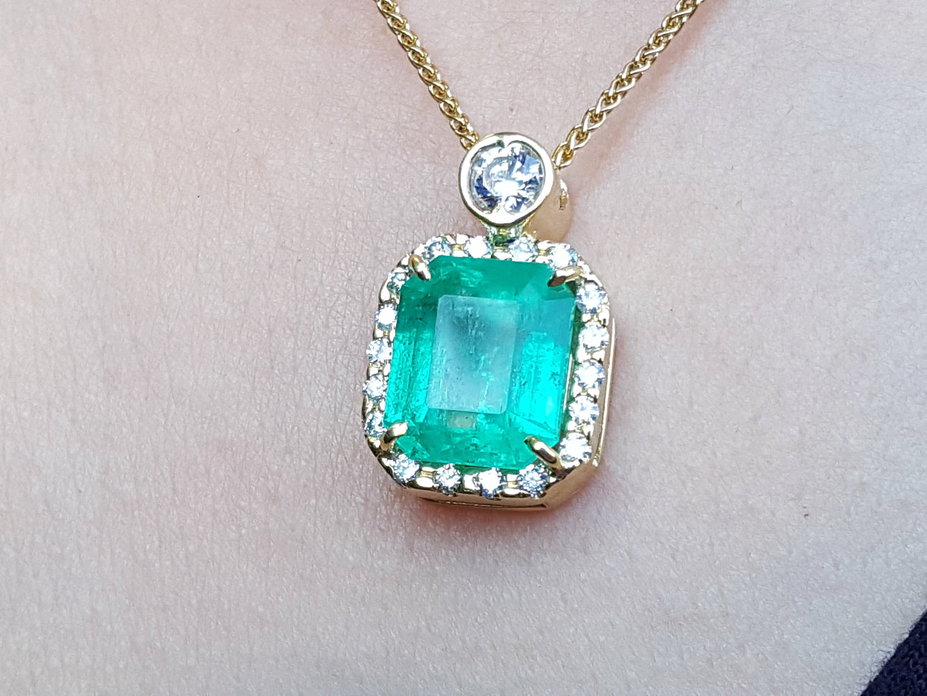 A square natural colombian emerald in a halo diamond pendant made in 18k yellow gold topside view.