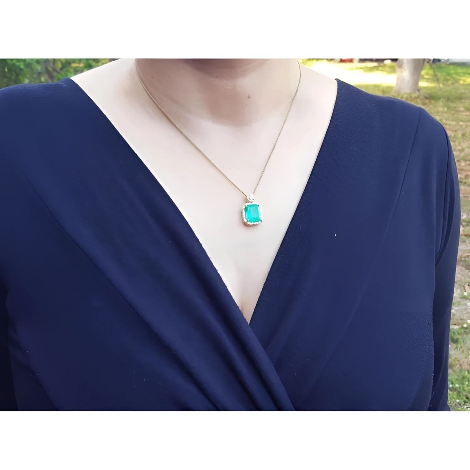 Emerald pendant necklace with diamond halo on an 18K yellow gold chain, worn on a woman's chest.