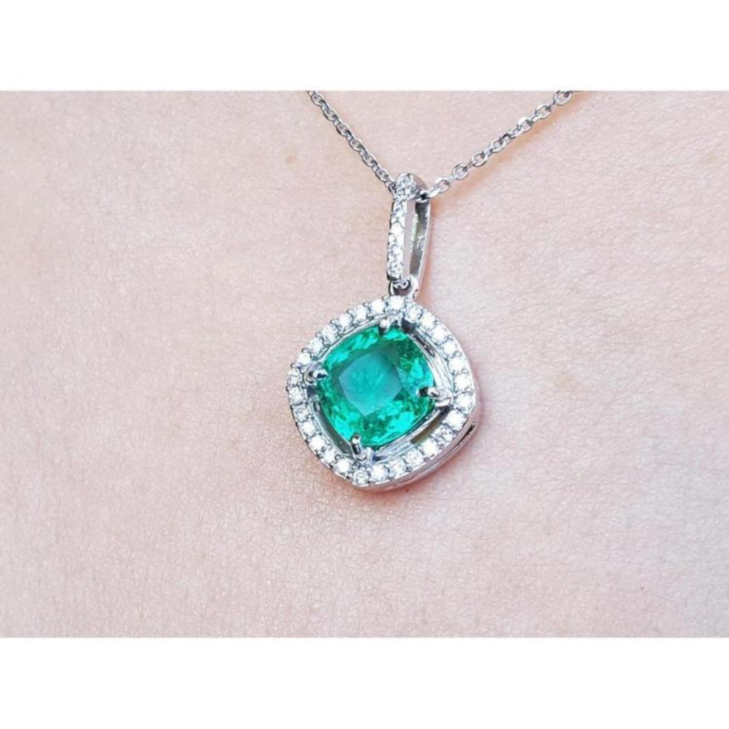 Natural emerald pendant cushion cut with halo diamond accents on a light pink skin background.
