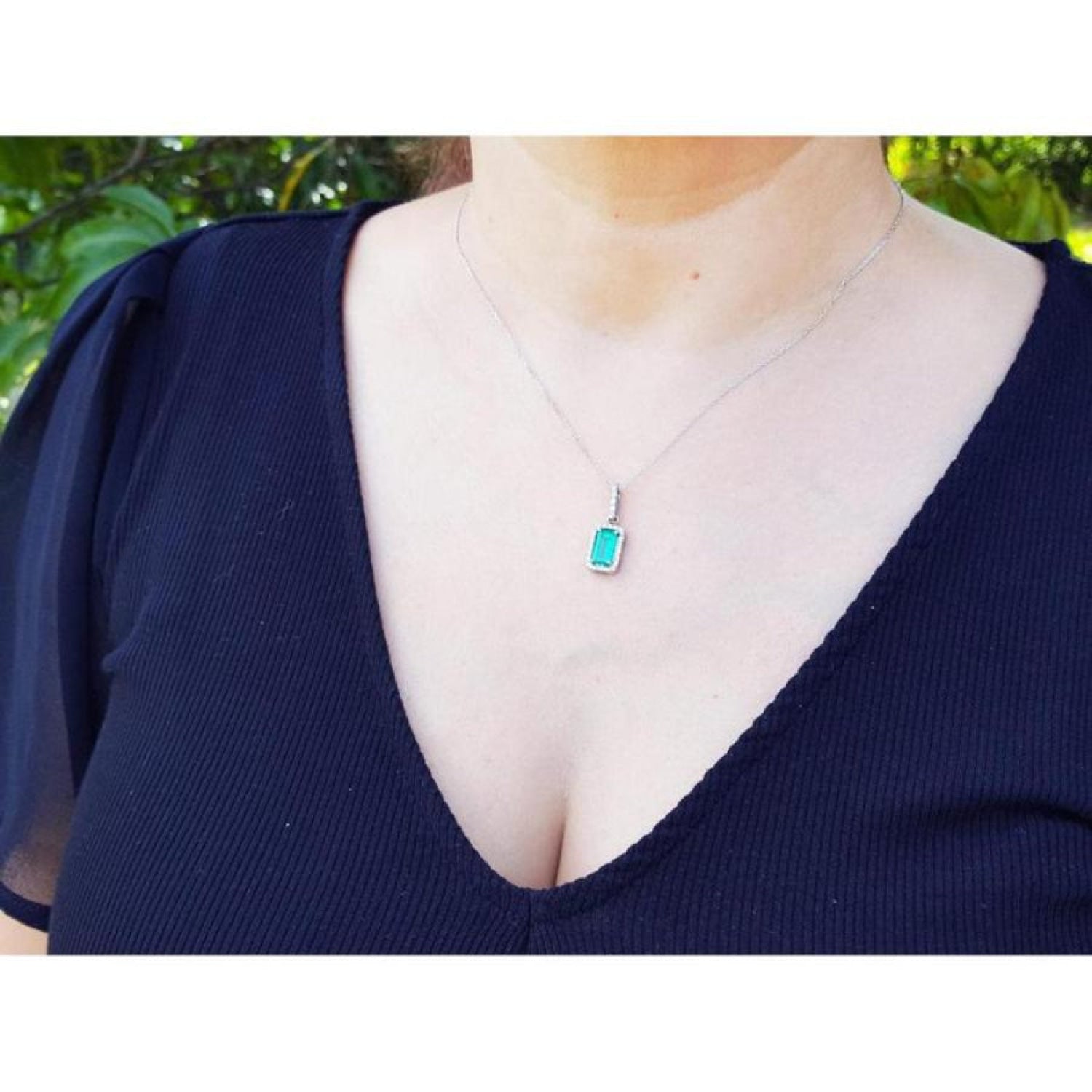 Woman wearing a 1.70 ct. Muzo Colombian emerald pendant with a diamond halo in 18K white gold.