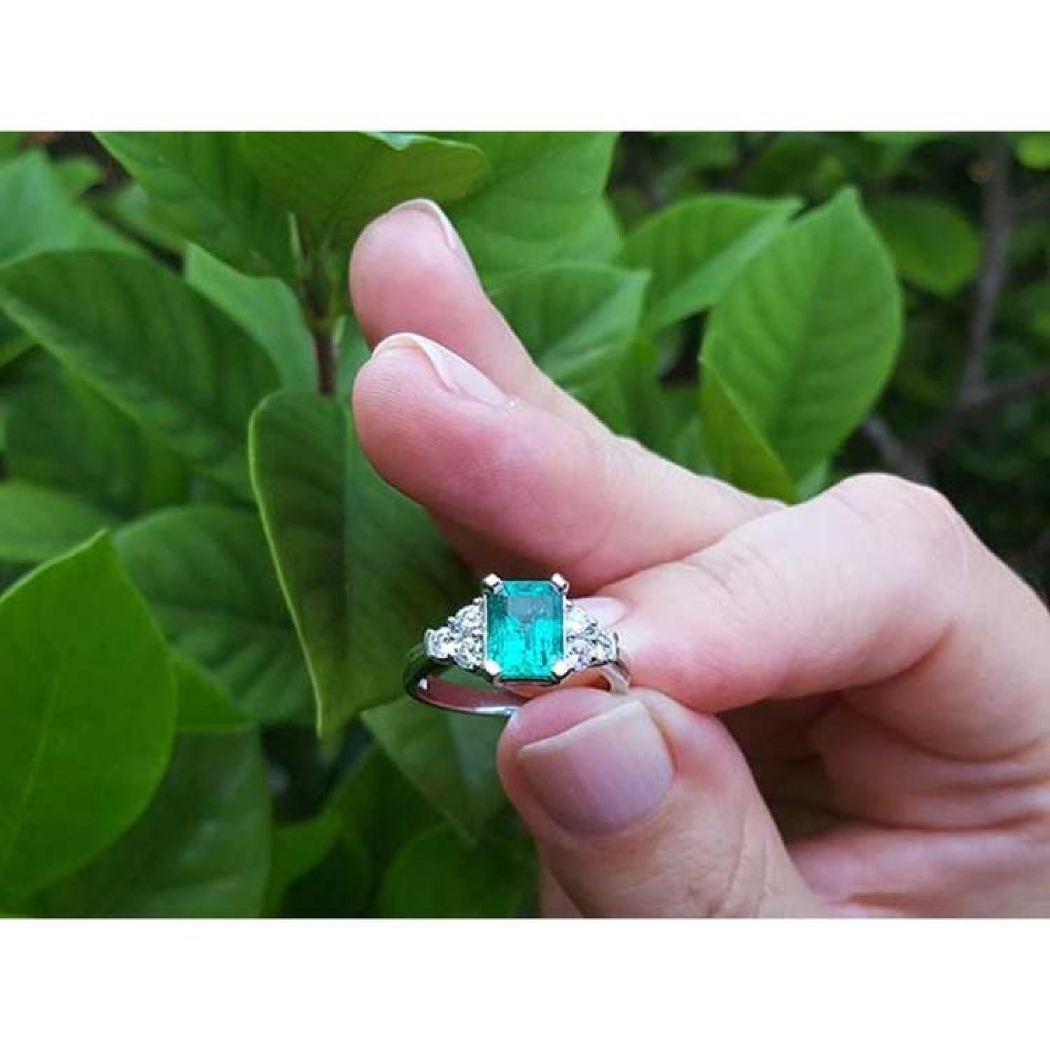 Emerald-cut vivid bluish green emerald ring with three diamonds on each side, set in white gold.