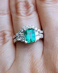 A real Colombian emerald and matching band ring on a finger against a natural background.