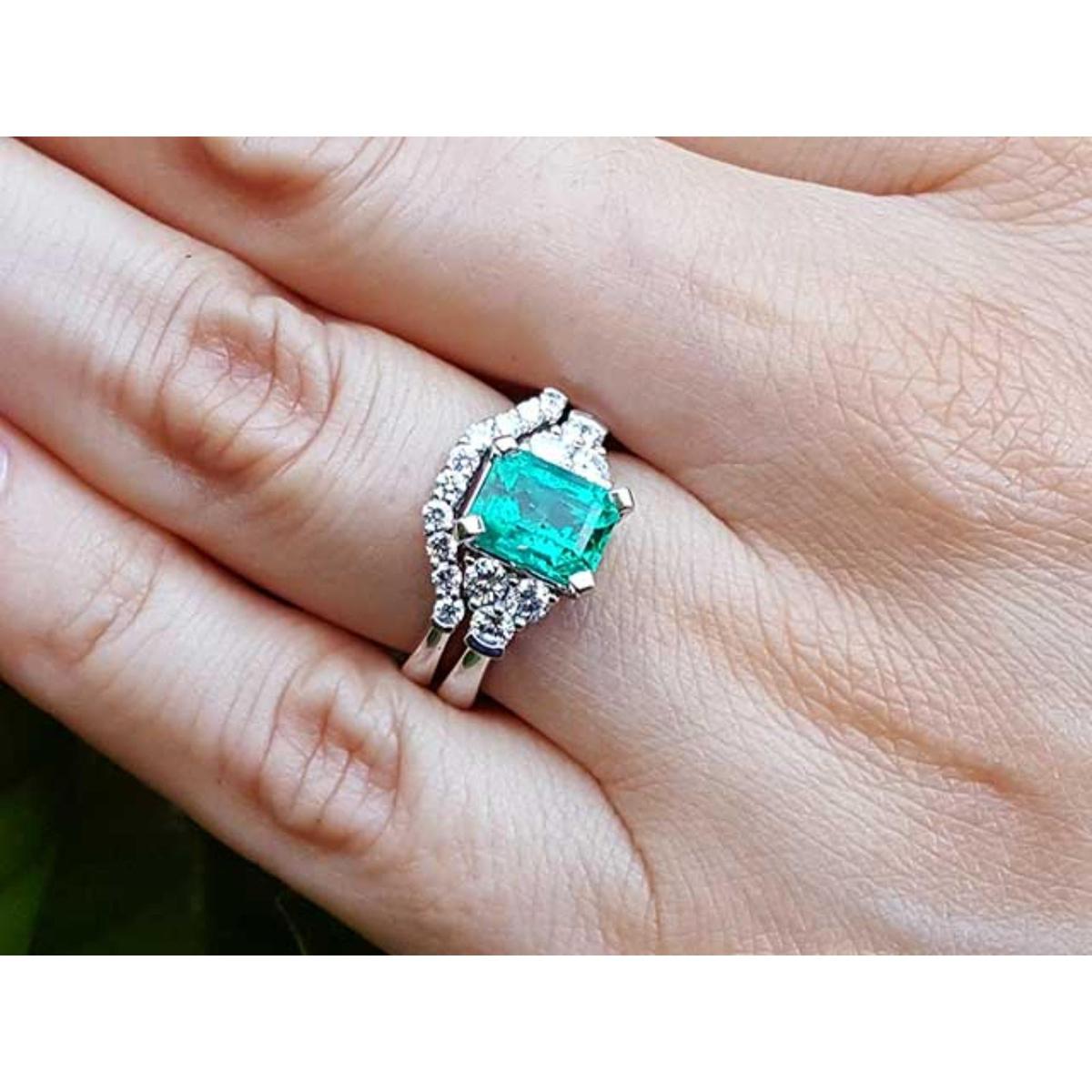 A Muzo born emerald on top of the ring with the matching wedding band on a person's finger.