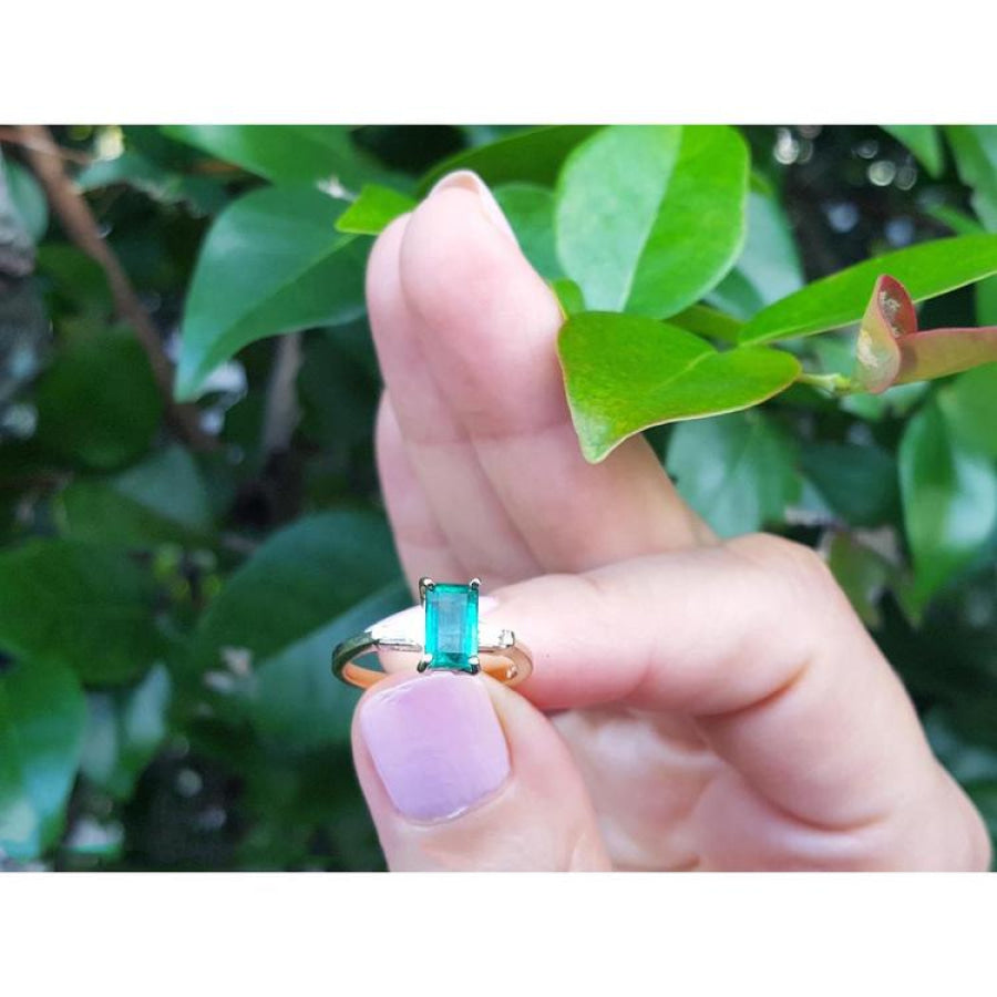 1.05 ct. natural emerald ring with side baguette diamonds in 14K yellow gold, worn on a finger.