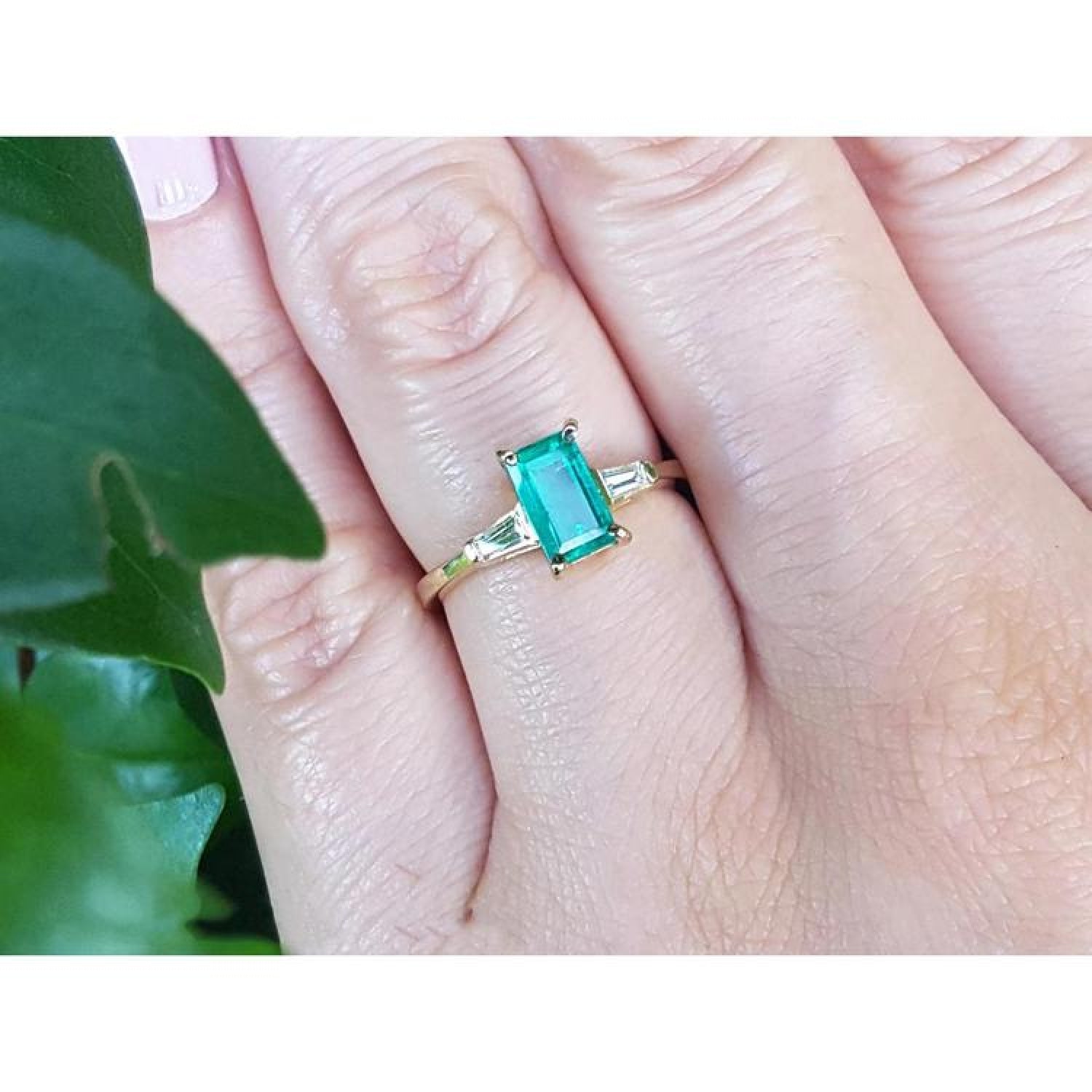 14K yellow gold ring with a rectangular emerald and side baguette diamonds on a hand.