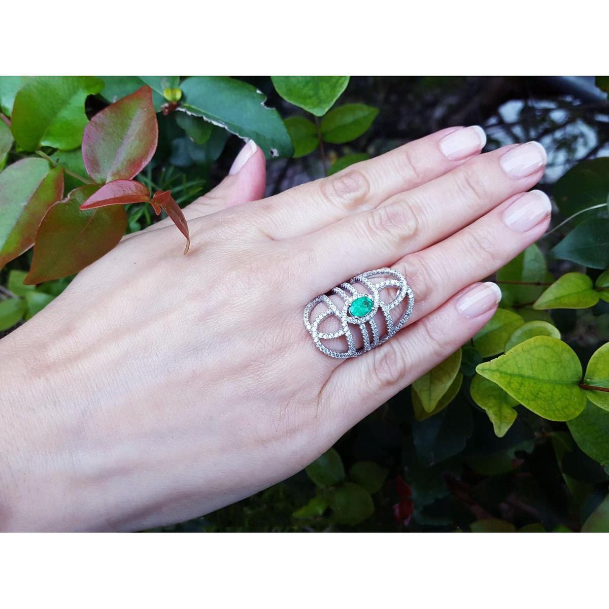 Hand wearing a silver ring with a real colombian emerald against a green leafy background.