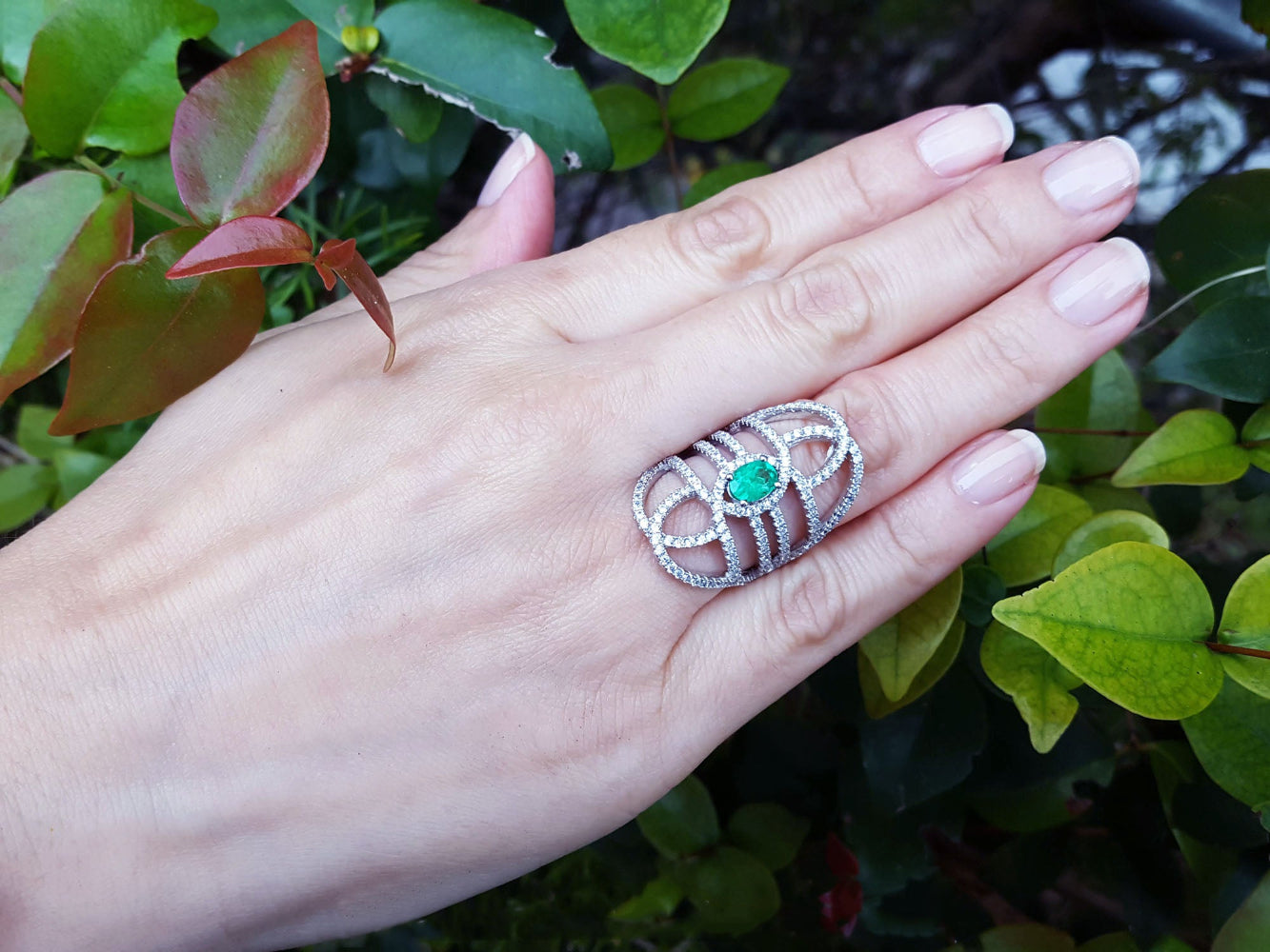 Hand wearing a silver ring with a real colombian emerald against a green leafy background.