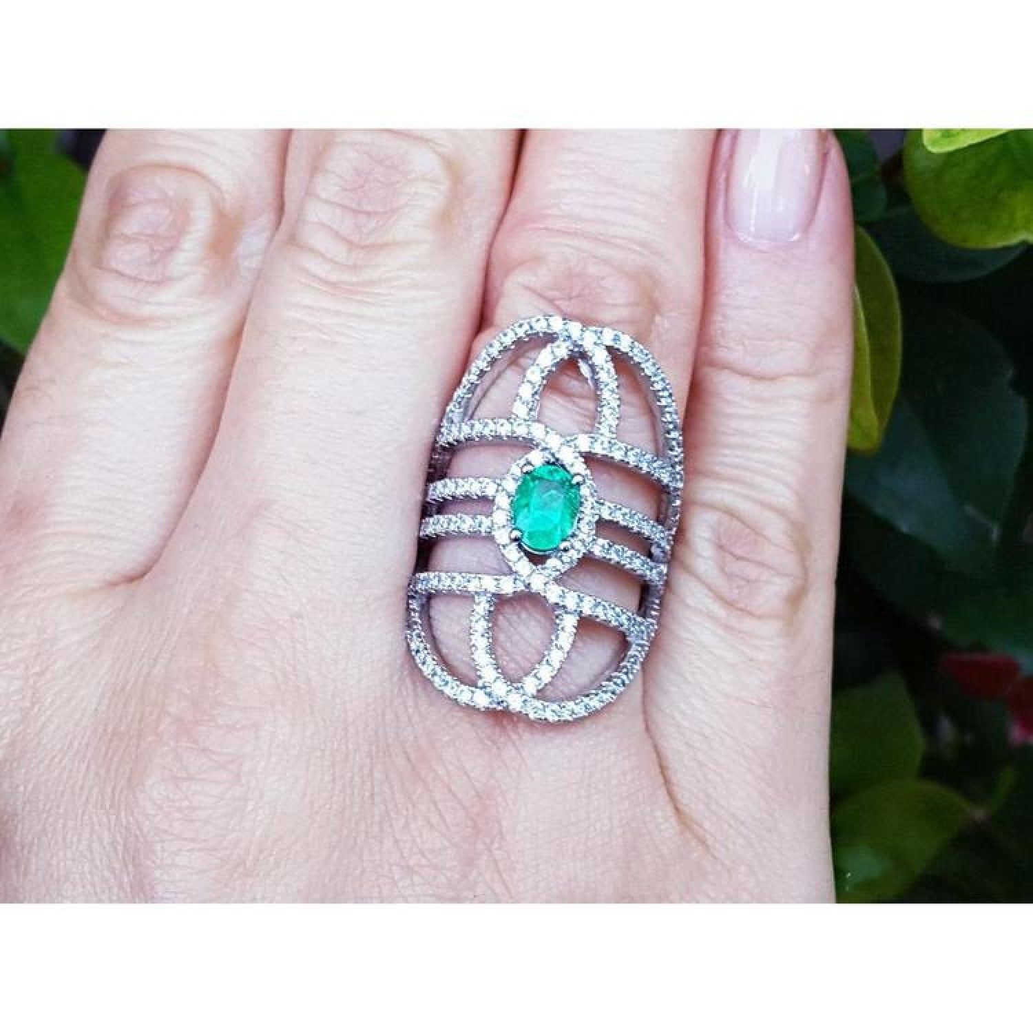 Sterling silver ring with oval natural emerald and CZ halo accent on a woman's finger.