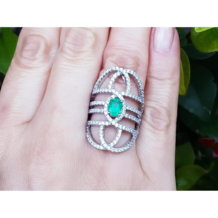 Sterling silver ring with oval natural emerald and CZ halo accent on a woman's finger.