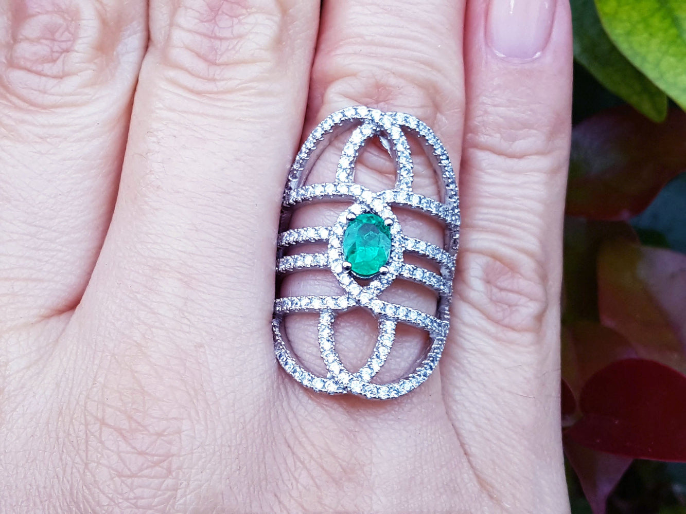 Silver ring with a natural oval emerald on a person's finger.