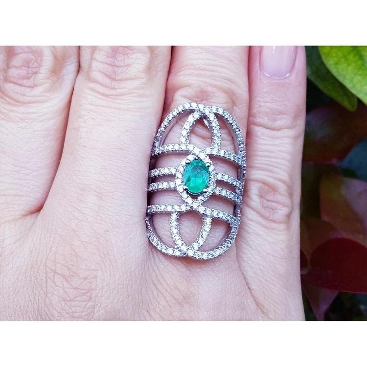 Silver ring with a natural oval emerald on a person's finger.