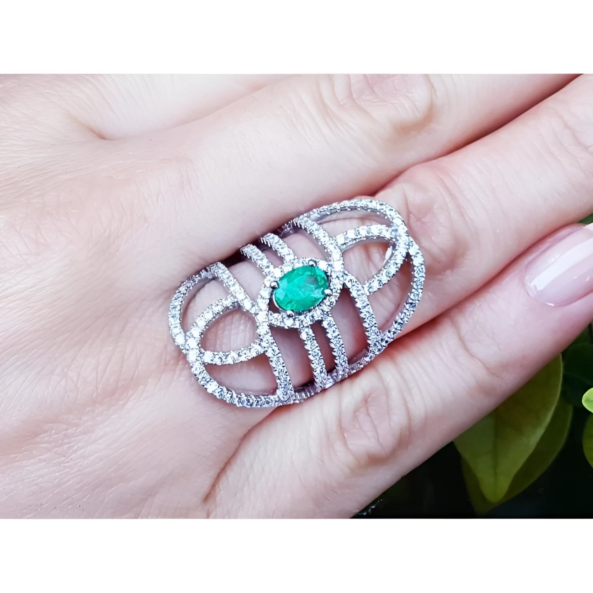 Sterling silver ring with a natural oval emerald center and CZ halo, featuring an intricate filigree design.