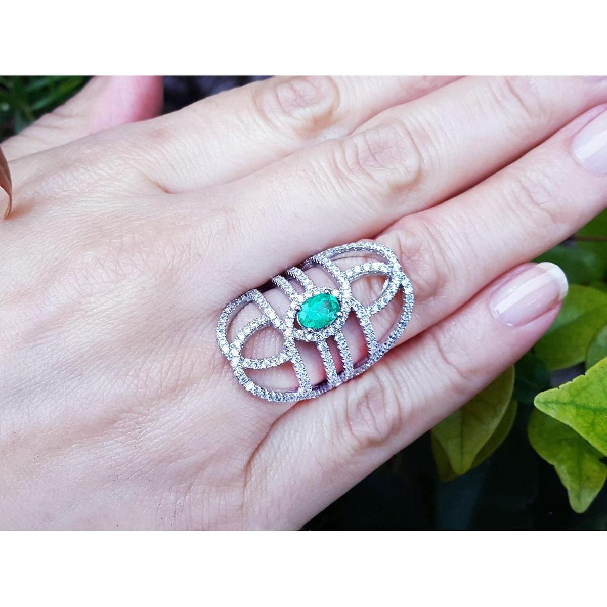Silver ring with a Muzo colombian emerald on a hand against a natural background.