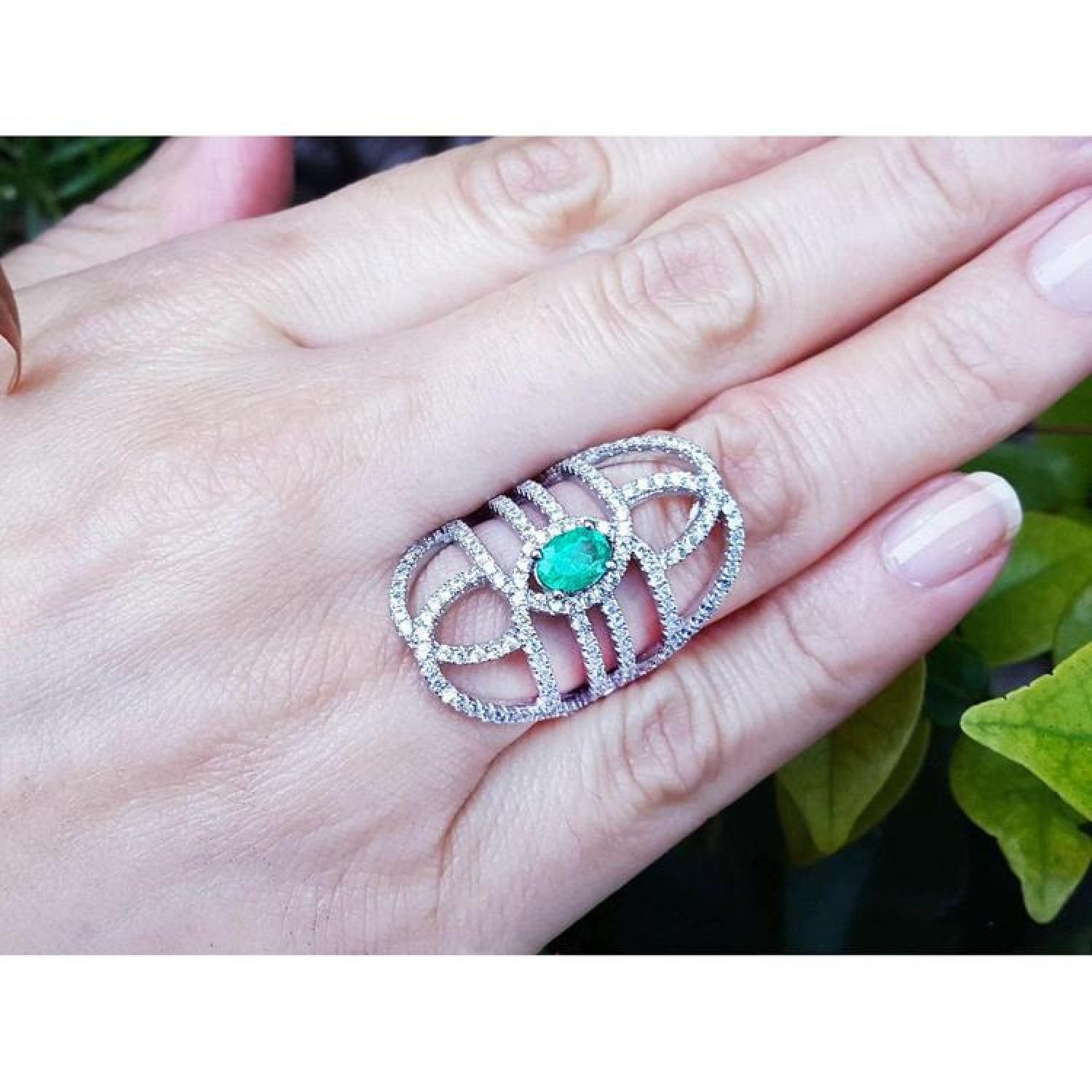 Sterling silver ring with oval emerald center and CZ halo on a woman's hand.